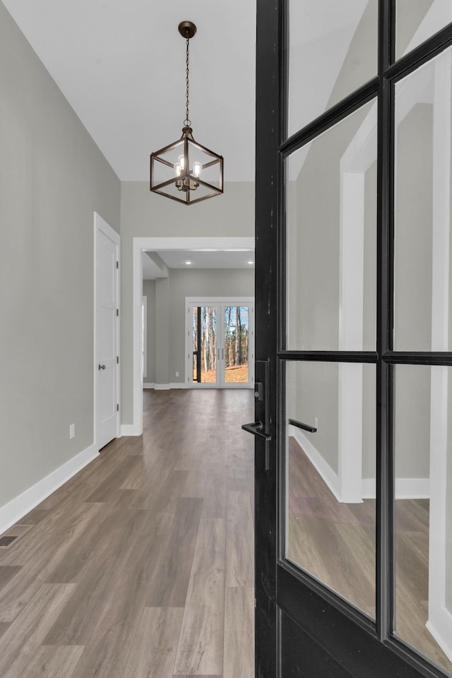 spare room with french doors, baseboards, an inviting chandelier, and wood finished floors