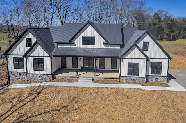 modern inspired farmhouse featuring a porch, a front lawn, stone siding, board and batten siding, and metal roof