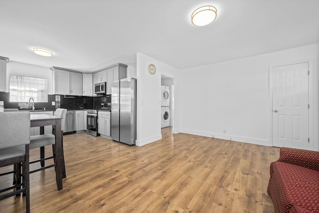 kitchen with stacked washer and clothes dryer, light wood-style flooring, gray cabinets, backsplash, and stainless steel appliances