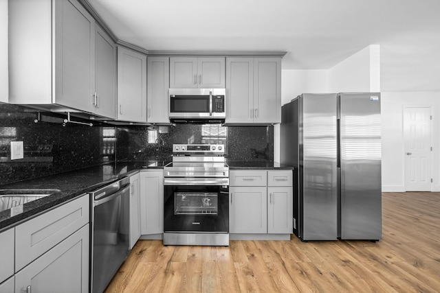 kitchen featuring gray cabinets, dark stone countertops, tasteful backsplash, stainless steel appliances, and light wood finished floors