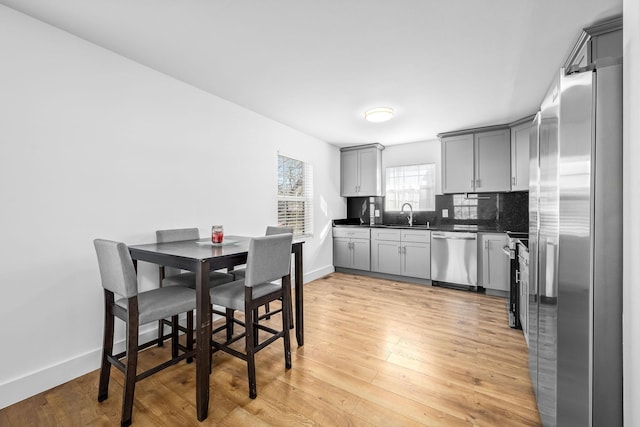 kitchen with dark countertops, gray cabinetry, decorative backsplash, light wood-style floors, and stainless steel appliances