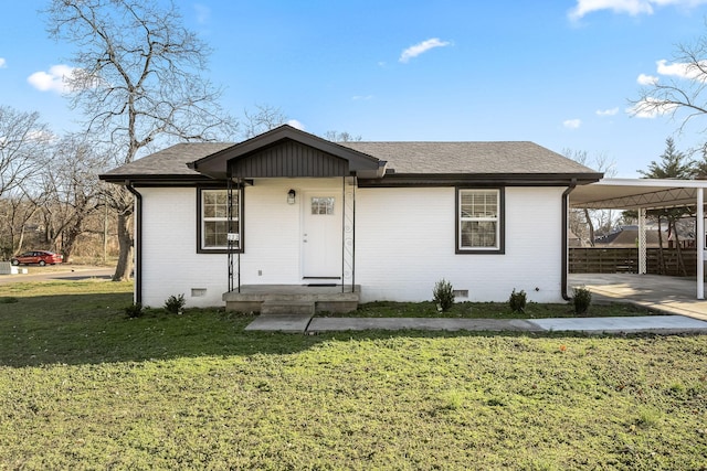 view of front facade with brick siding, an attached carport, a shingled roof, a front yard, and crawl space