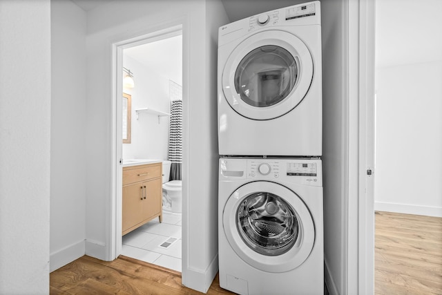 washroom with light wood finished floors, stacked washer / dryer, laundry area, and baseboards