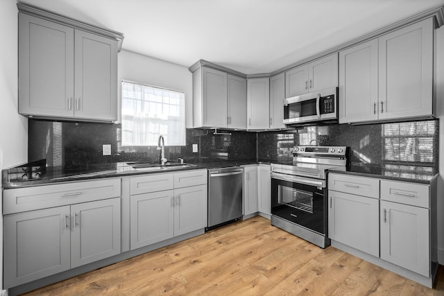 kitchen featuring gray cabinetry, decorative backsplash, light wood-style flooring, appliances with stainless steel finishes, and a sink