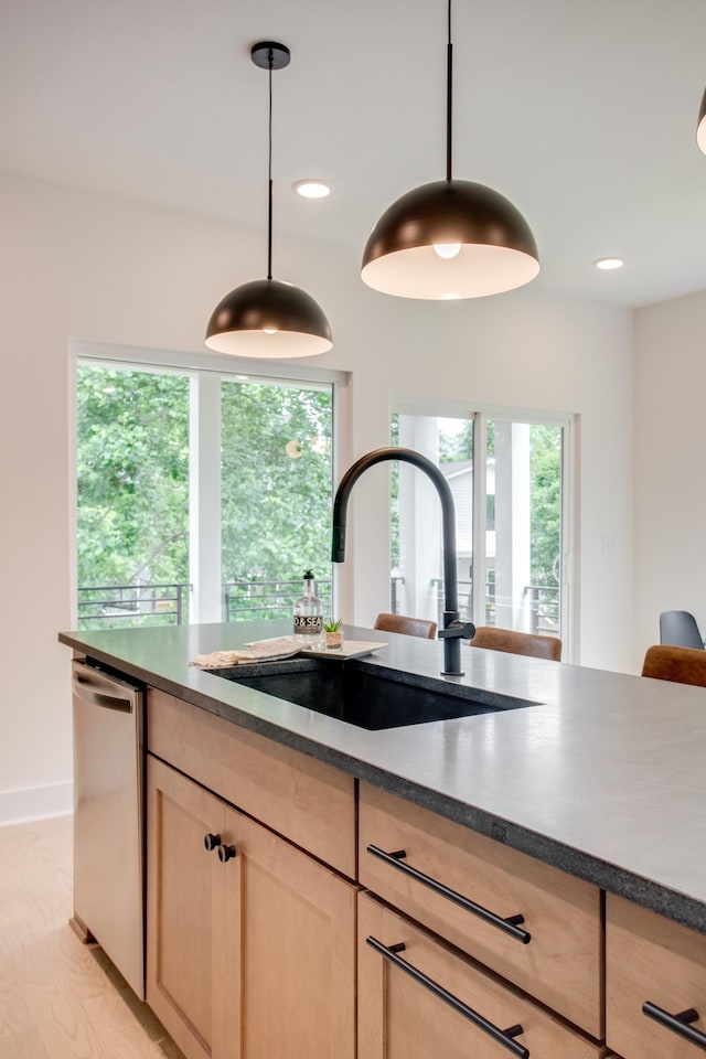 kitchen featuring dark countertops, light brown cabinetry, dishwasher, recessed lighting, and a sink