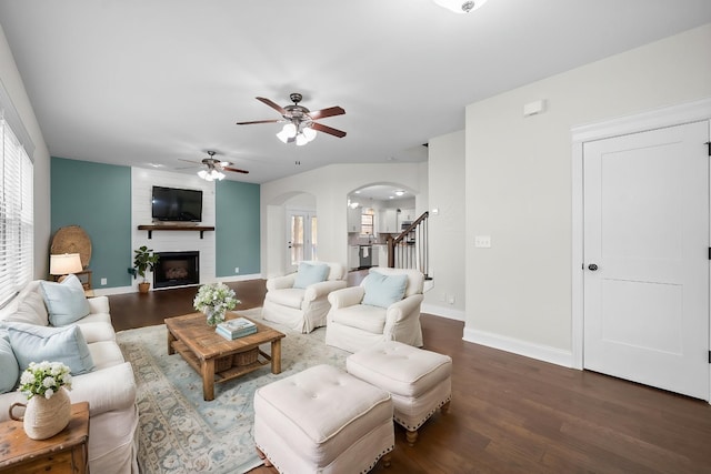 living room with dark wood-style floors, arched walkways, a fireplace, baseboards, and stairs