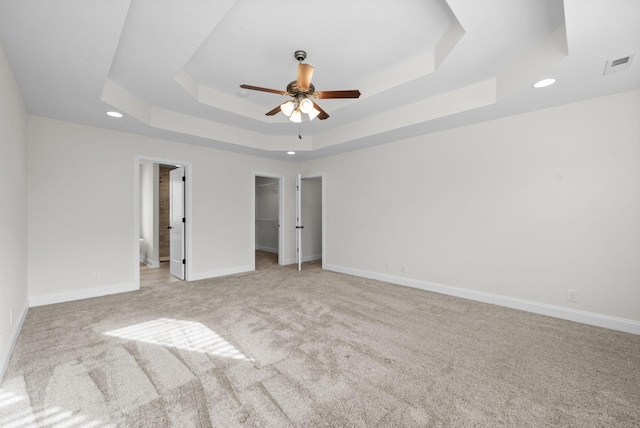 unfurnished bedroom featuring a spacious closet, visible vents, baseboards, a tray ceiling, and carpet floors