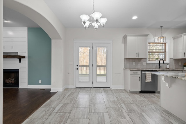 kitchen with backsplash, light stone countertops, stainless steel dishwasher, and a fireplace