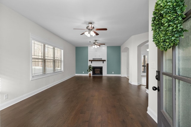 unfurnished living room with baseboards, arched walkways, dark wood-style flooring, and a fireplace