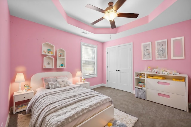 bedroom with a ceiling fan, baseboards, carpet floors, a closet, and a raised ceiling