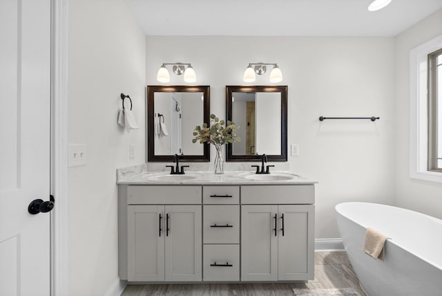 bathroom featuring a freestanding bath, double vanity, baseboards, and a sink