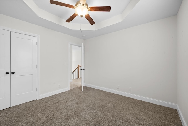 unfurnished bedroom featuring a closet, carpet flooring, baseboards, and a tray ceiling