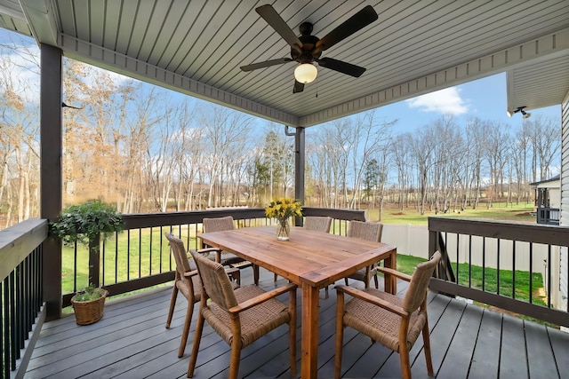 wooden deck featuring outdoor dining space, a ceiling fan, and a lawn