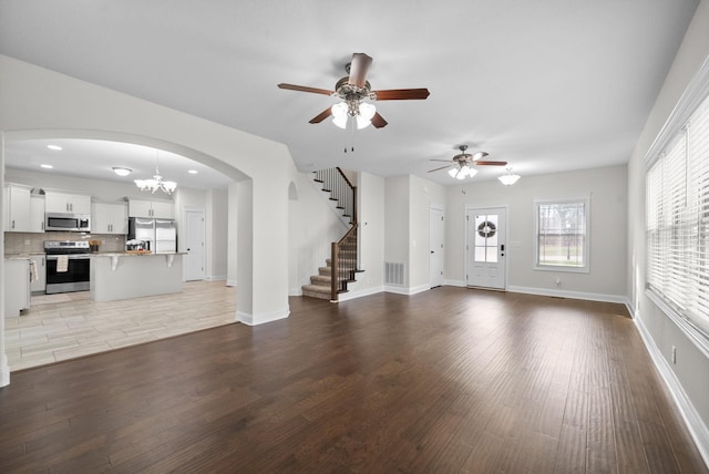 unfurnished living room with stairway, wood finished floors, baseboards, visible vents, and arched walkways