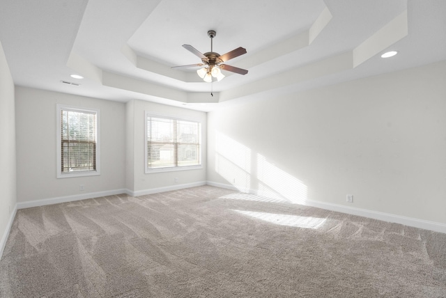 empty room with baseboards, a raised ceiling, light carpet, and ceiling fan