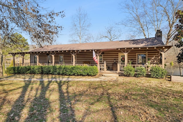 back of property with log siding, covered porch, roof with shingles, and a chimney