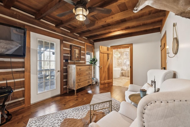 living area featuring beamed ceiling, wood ceiling, ceiling fan, and dark wood-style flooring