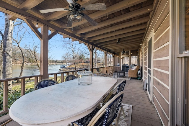 deck with outdoor dining area, a ceiling fan, and a water view