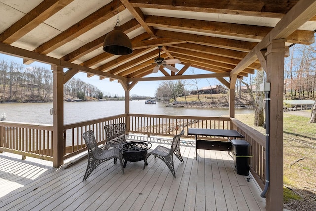 wooden deck with a gazebo, a water view, ceiling fan, and an outdoor fire pit