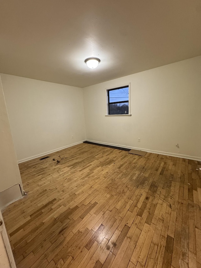 spare room with baseboards, visible vents, and wood-type flooring