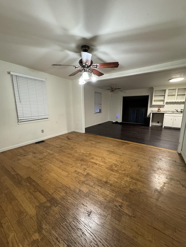 unfurnished living room with visible vents, a ceiling fan, dark wood-type flooring, and baseboards