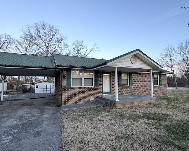 ranch-style house featuring fence, a carport, aphalt driveway, brick siding, and metal roof