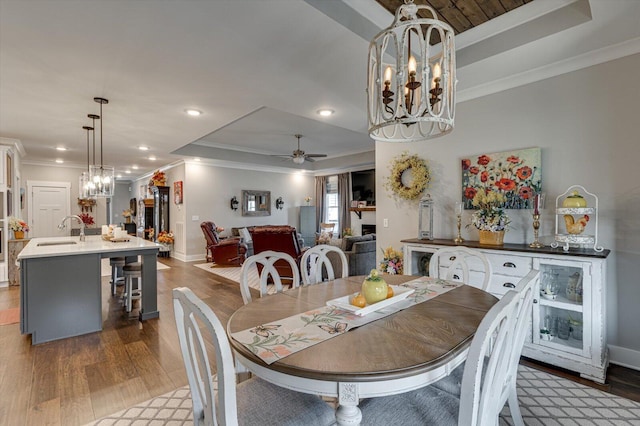 dining room featuring ceiling fan with notable chandelier, a tray ceiling, crown molding, and wood finished floors