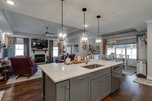 kitchen featuring a sink, gray cabinetry, a large fireplace, a raised ceiling, and stainless steel dishwasher