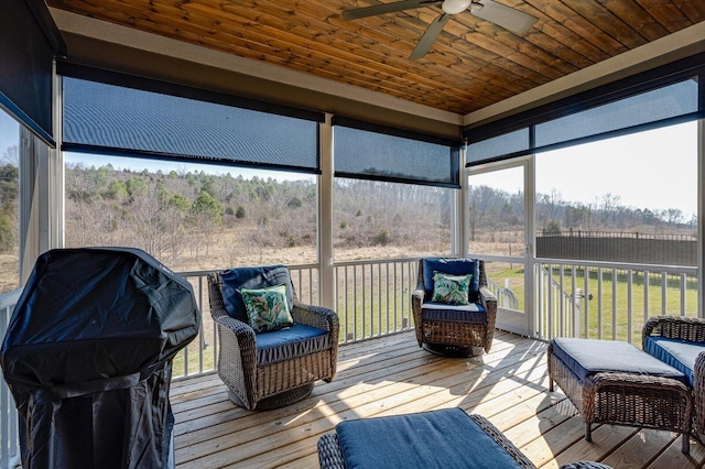 sunroom / solarium with wood ceiling, a wooded view, and ceiling fan