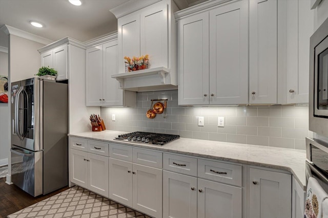 kitchen featuring light wood-style flooring, ornamental molding, stainless steel appliances, white cabinets, and backsplash