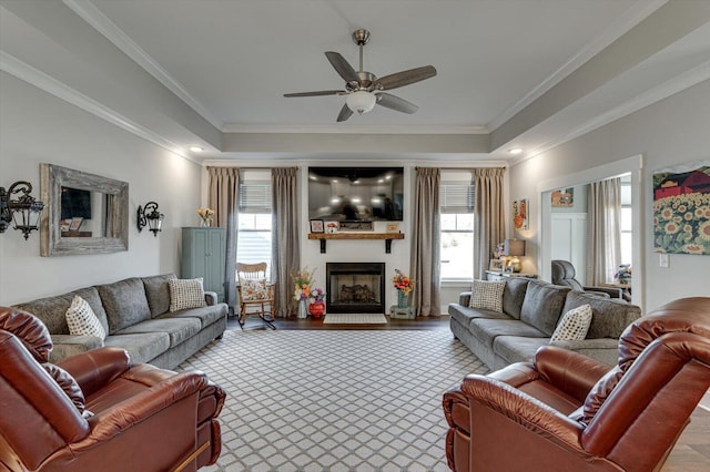 living area with a ceiling fan, a raised ceiling, a fireplace, and ornamental molding