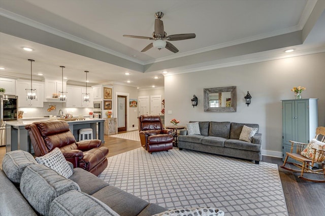 living area with baseboards, a tray ceiling, recessed lighting, dark wood-style flooring, and ornamental molding