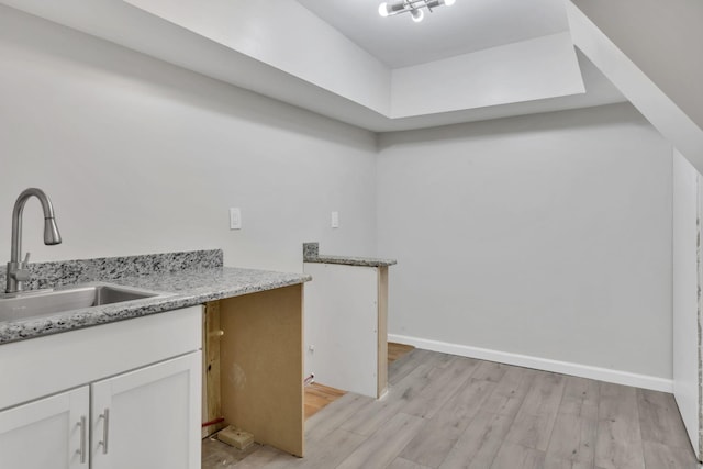 kitchen with light wood finished floors, baseboards, light stone counters, white cabinets, and a sink