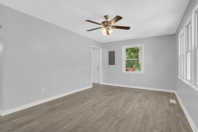 empty room featuring electric panel, ceiling fan, baseboards, and light wood-style floors