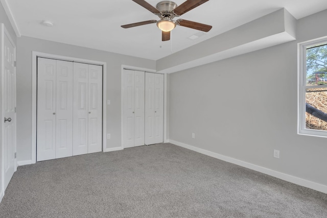 unfurnished bedroom with a ceiling fan, carpet flooring, baseboards, and multiple closets