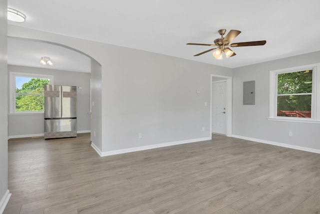 unfurnished room featuring electric panel, arched walkways, baseboards, and wood finished floors