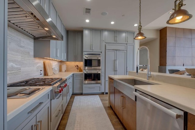 kitchen featuring visible vents, gray cabinets, stainless steel appliances, light countertops, and wall chimney exhaust hood