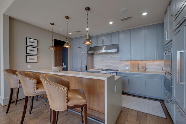 kitchen with wood finished floors, visible vents, light countertops, under cabinet range hood, and tasteful backsplash