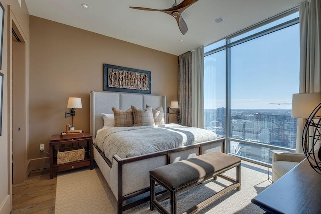 bedroom featuring expansive windows, a city view, wood finished floors, and a ceiling fan