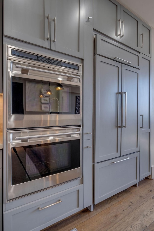 kitchen with light wood-style floors, double oven, paneled fridge, and gray cabinetry