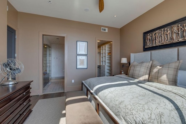 bedroom featuring visible vents, a walk in closet, ensuite bathroom, wood finished floors, and baseboards