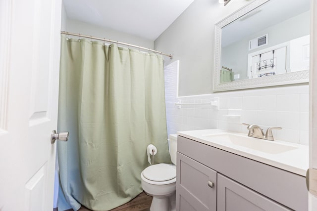 bathroom featuring vanity, a wainscoted wall, visible vents, tile walls, and toilet