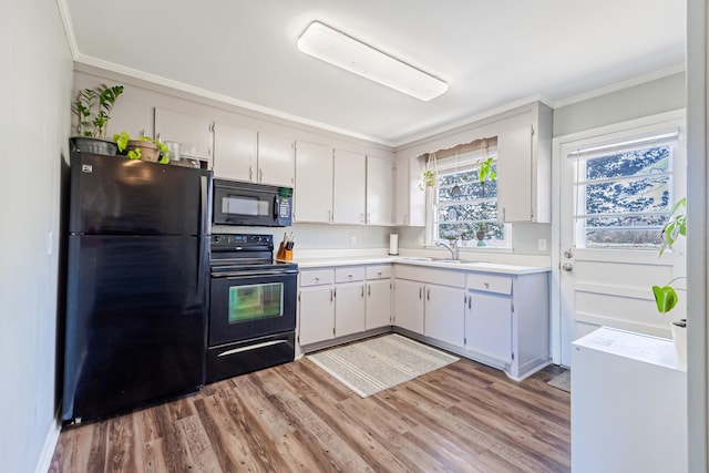 kitchen featuring black appliances, ornamental molding, a sink, light wood-style floors, and light countertops