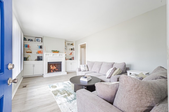 living room featuring light wood finished floors, visible vents, a fireplace, and built in features