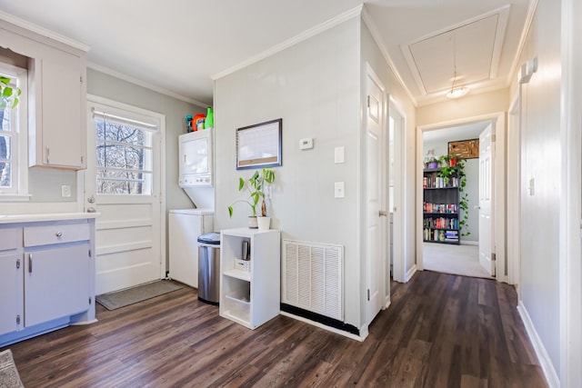 kitchen featuring visible vents, dark wood-type flooring, stacked washing maching and dryer, crown molding, and light countertops