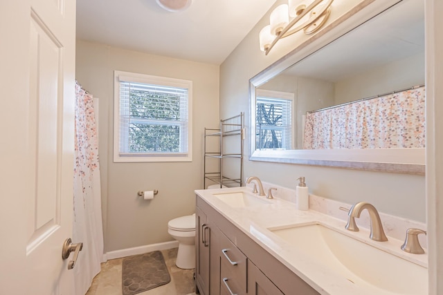 bathroom featuring double vanity, toilet, baseboards, and a sink