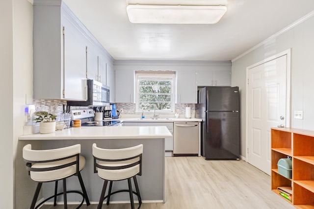 kitchen featuring a peninsula, ornamental molding, a sink, light countertops, and appliances with stainless steel finishes