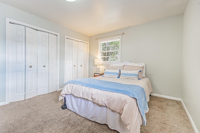 carpeted bedroom featuring baseboards and two closets