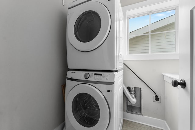 clothes washing area featuring laundry area, stacked washing maching and dryer, baseboards, and wood finished floors