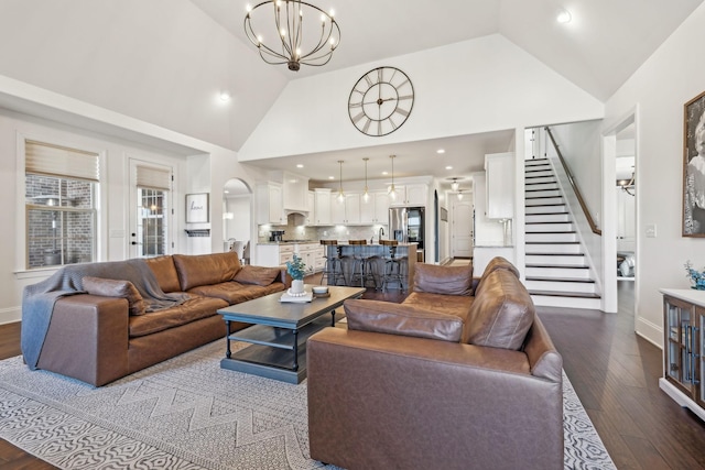 living room with stairway, dark wood-type flooring, high vaulted ceiling, and a notable chandelier